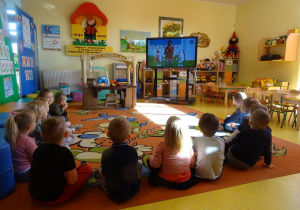 Dzieci siedzą w półkolu i oglądają film edukacyjny.